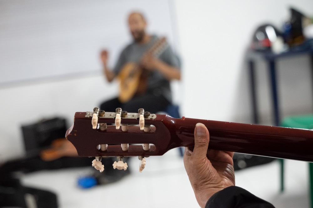 una persona toca guitarra. A l fondo se ve al profesor